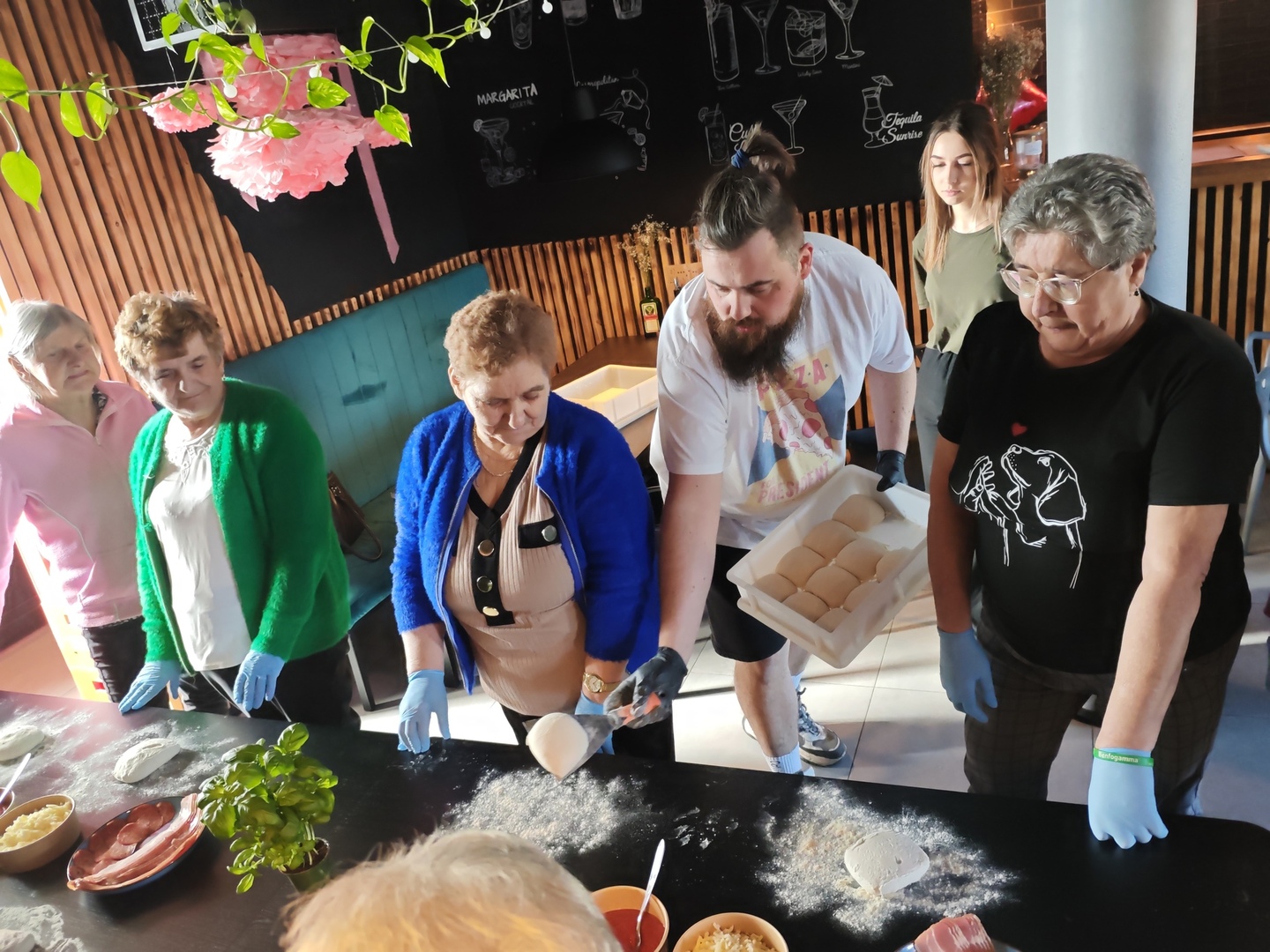 Zdjęcie przedstawia seniorów wykonujących pizze podczas warsztatów kulinarnych zorganizowanych w restauracji graj w zielone