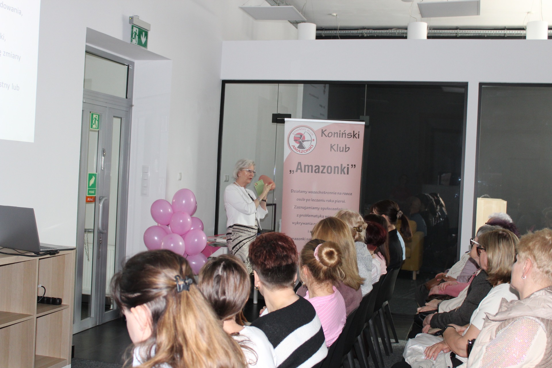 Zdjęcie przedstawia słuchaczy oraz Panią z Konińskiego Klubu Amazonki, która przy użyciu fantomu piersi demonstruje sposoby wykonywania samobadania piersi.