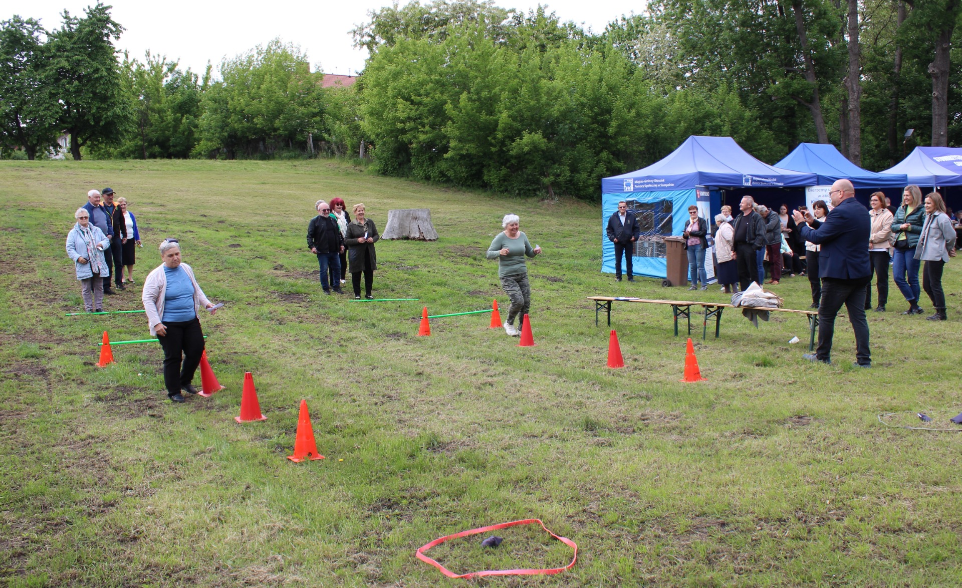 Zdjęcie przedstawia uczestników konkurencji ruchowej zorganizowanej podczas Majówki Seniora, którzy mierzą się z przygotowanym torem przeszkód