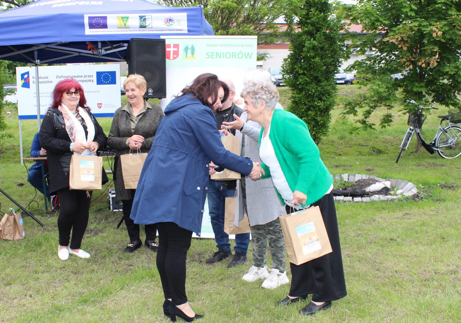 Zdjęcie przedstawia Panią Anetę Niestrawską – Sekretarz Gminy Sompolno, która wręcza Seniorce nagrody za udział w konkursach i zabawach zorganizowanych na majówce.