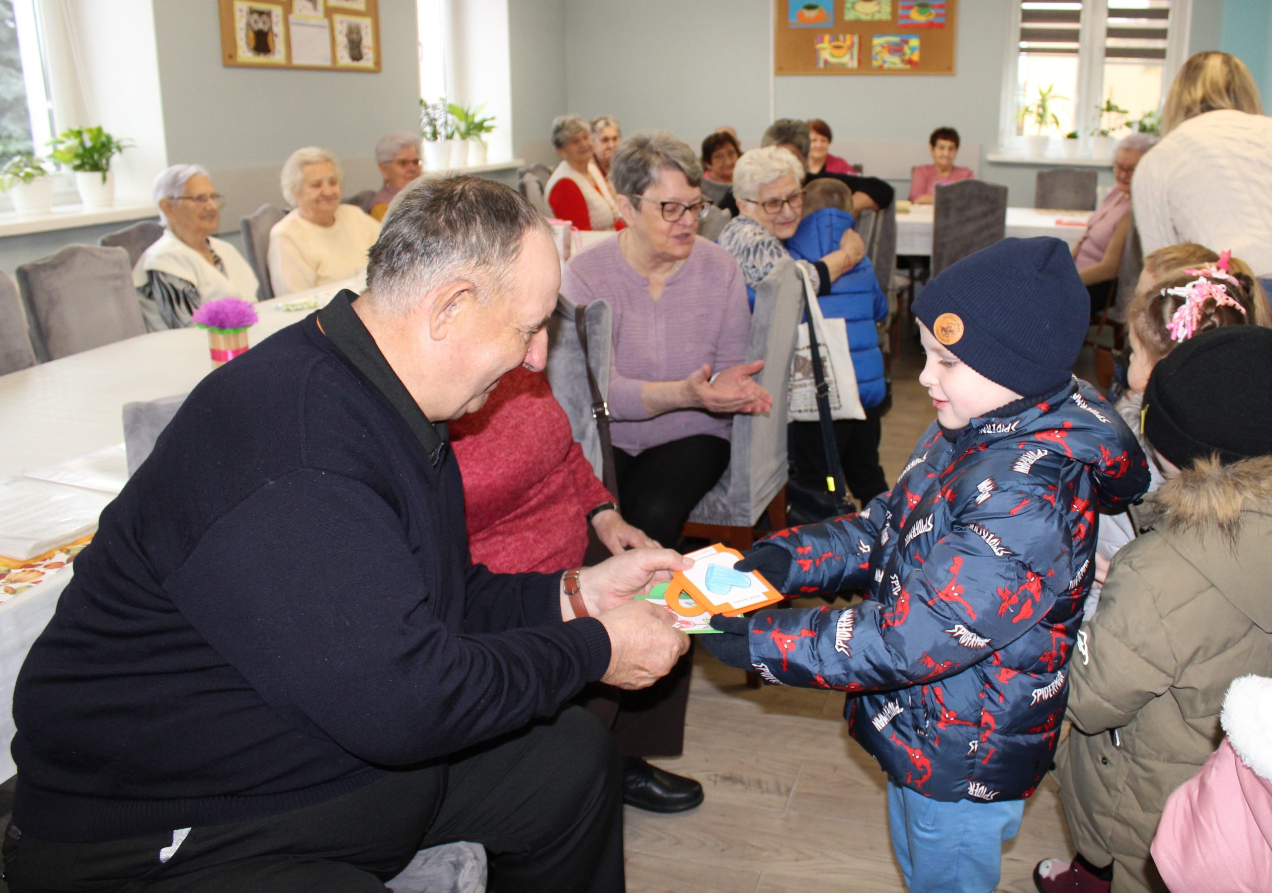 2. Zdjęcie przedstawia chłopca wręczającego seniorowi laurkę