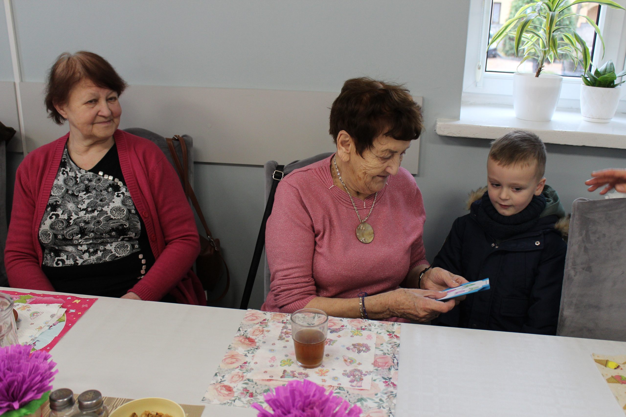 3. Zdjęcie przedstawia chłpca wręczającego seniorce laurkę