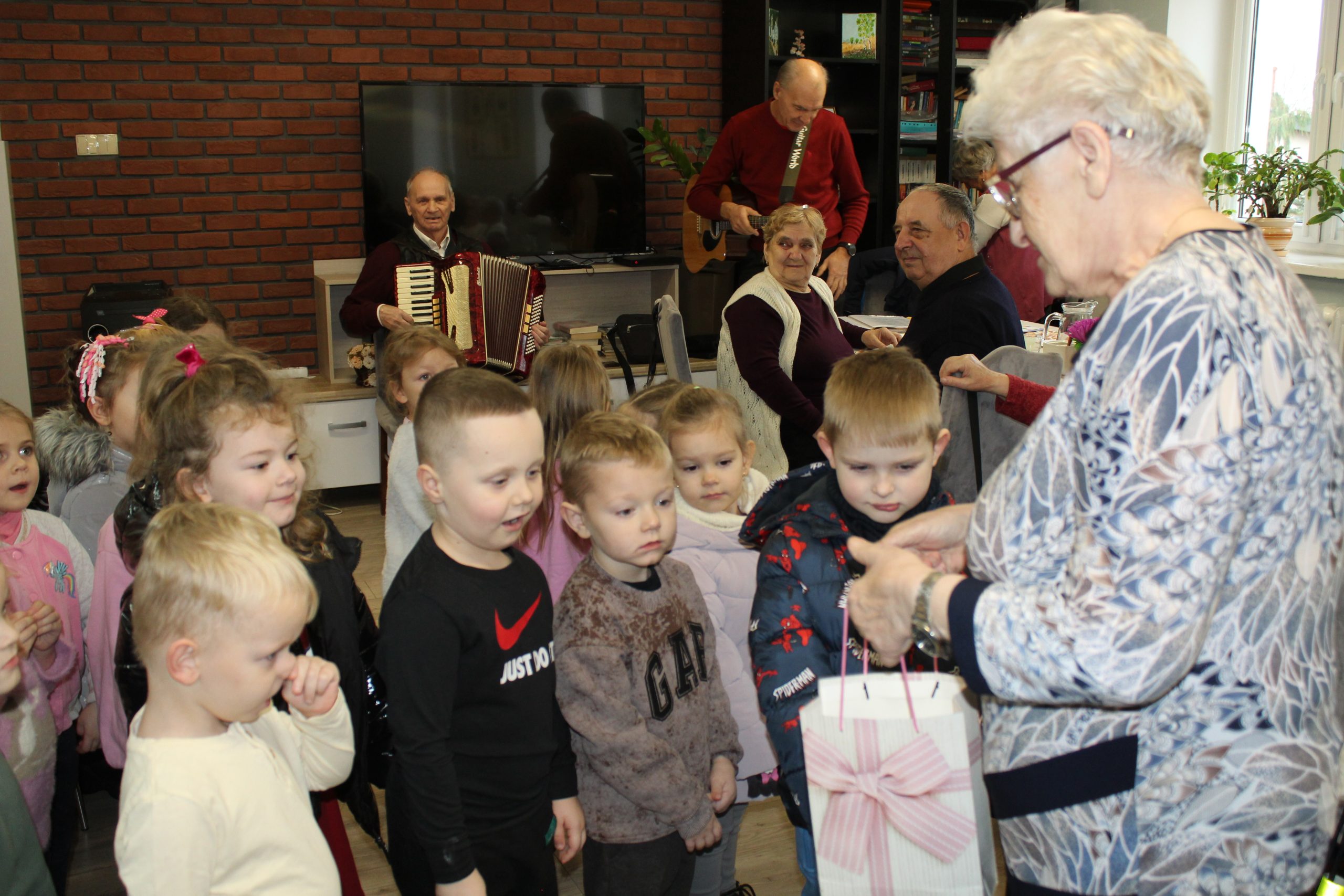 4. Zdjęcie przedstawia seniorkę wręczającą dzieciom słodki upominek.