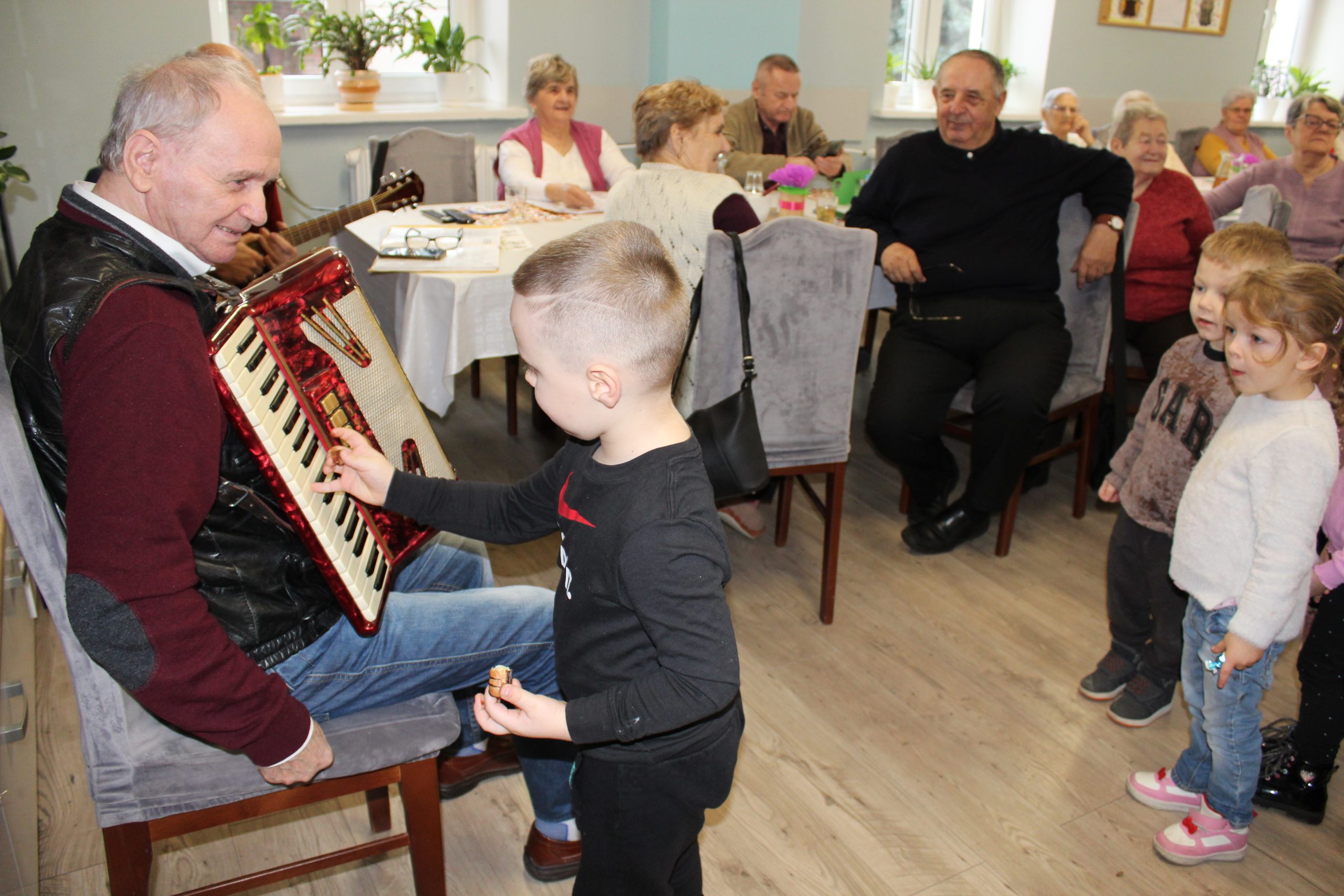 5. Na fotografii widzimy przedszkolaka, który podszedł do seniora grającego na akordeonie by zobaczyć instrument muzyczny.