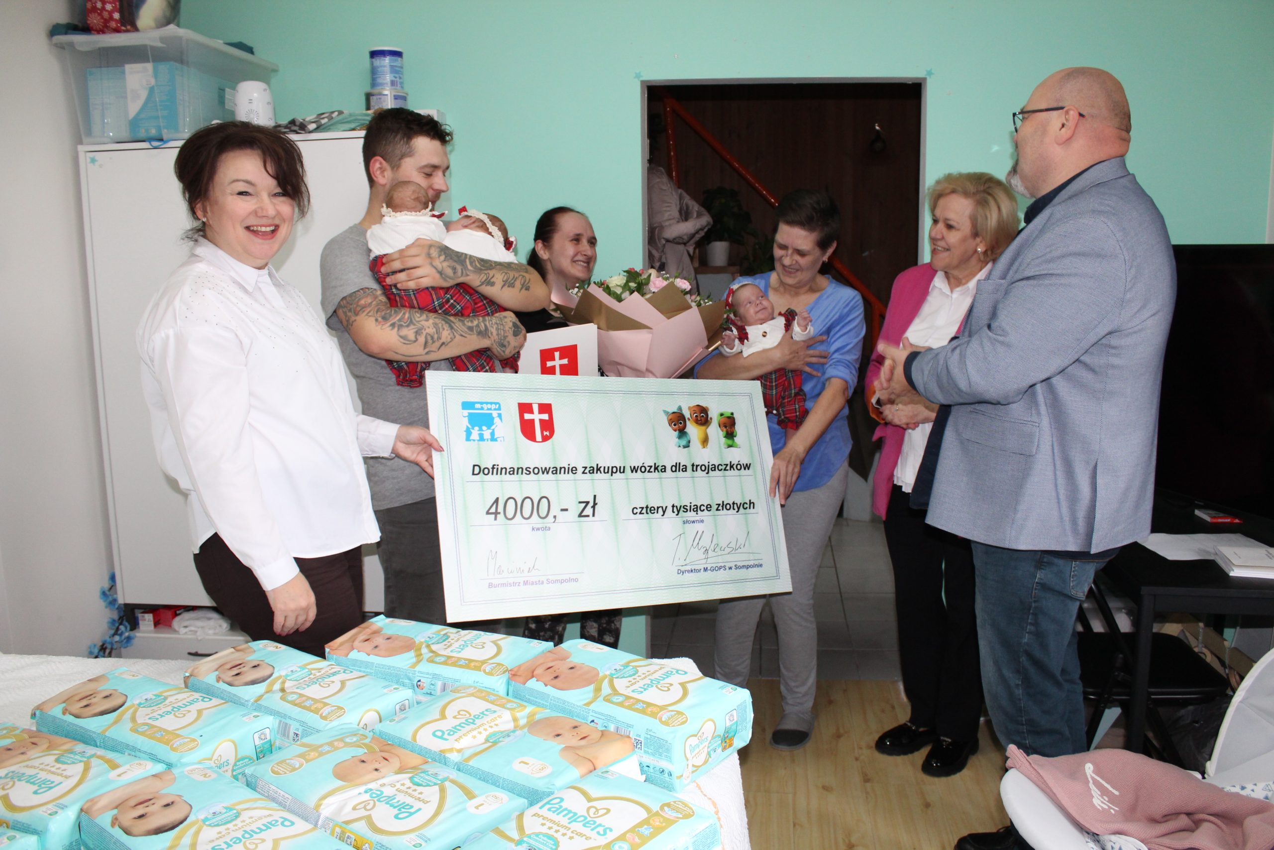 2) Zdjęcie przedstawia moment wręczenia rodzinie dofinansowania na zakup wózka dla trojaczków