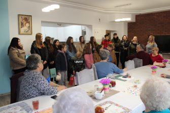 1) Zdjęcie wykonane w Domu Dziennego Pobytu. Przedstawia uczniów wraz z opiekunami, którzy przybyli do seniorów oraz pracownicę MGOPS w Sompolnie witającą uczniów.