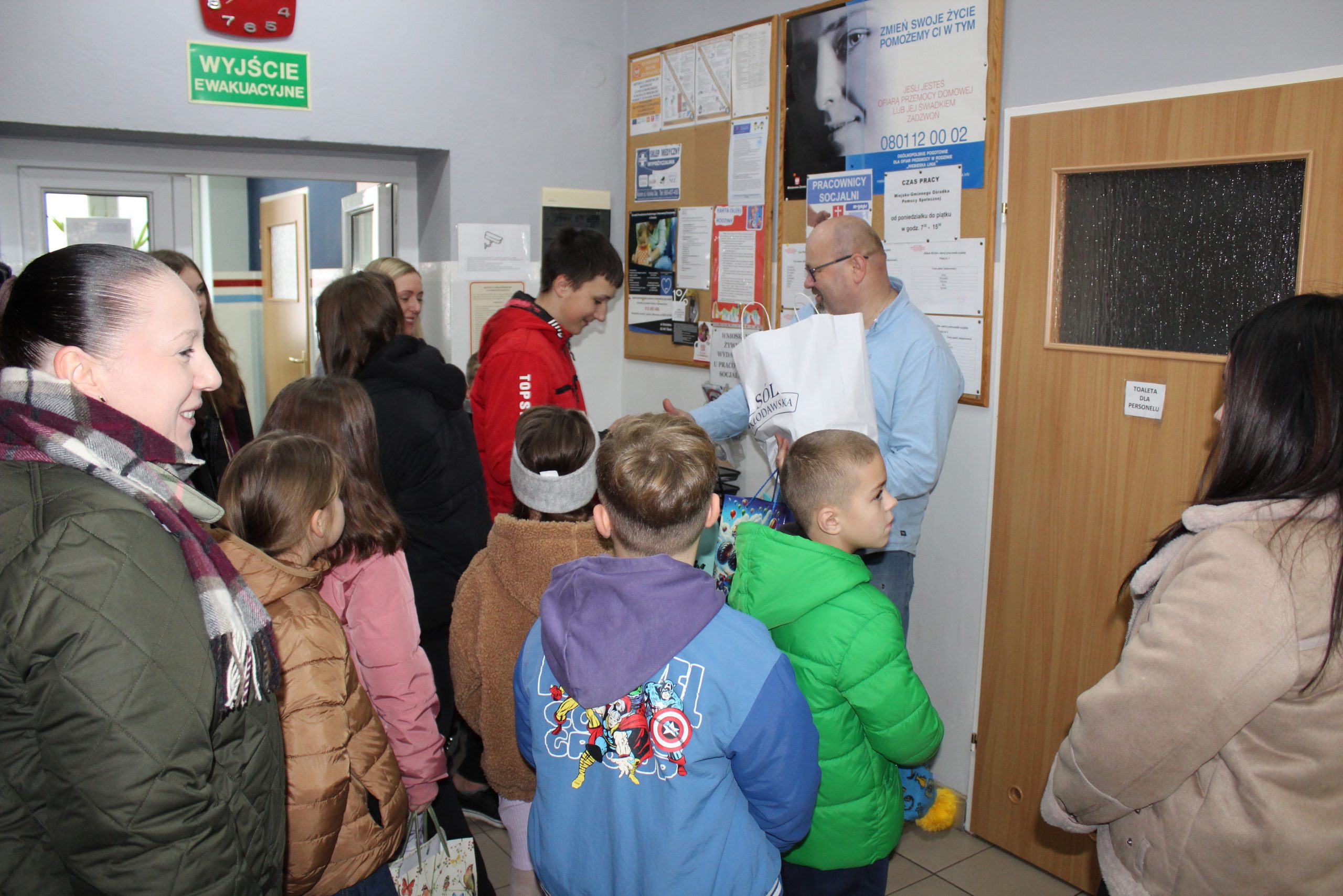 3) Zdjęcie wykonane w pomieszczeniu MGOPS w Sompolnie. Przedstawia ucznia wręczającego Dyrektorowi – Tomaszowi Majewskiemu słodycze dla seniorów z gminy.