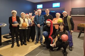 1) Zdjęcie grupowe wykonane na kręgielni. Przedstawia seniorów i opiekunów z kulami do kręgli.