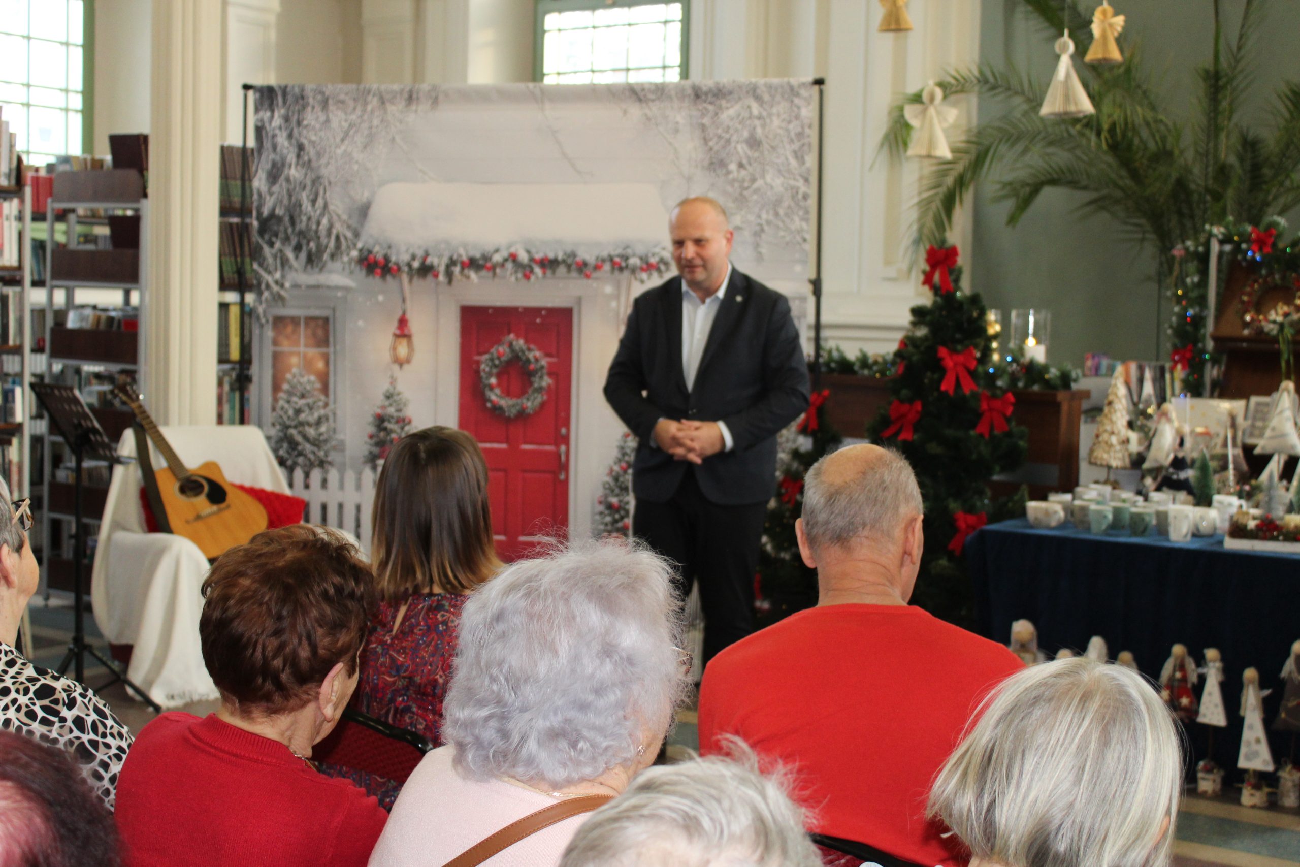 1) Zdjęcie wykonane w Miejsko – Gminnej Bibliotece Publicznej w Sompolnie. Przedstawia Burmistrza otwierającego wystawę świąteczną. Przed nim siedzą uczestnicy spotkania.