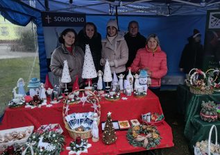 1) Zdjęcie wykonane podczas kiermaszu bożonarodzeniowego. Przedstawia pracowników przy stoisku DDP. Przed nimi stół z rękodziełem.