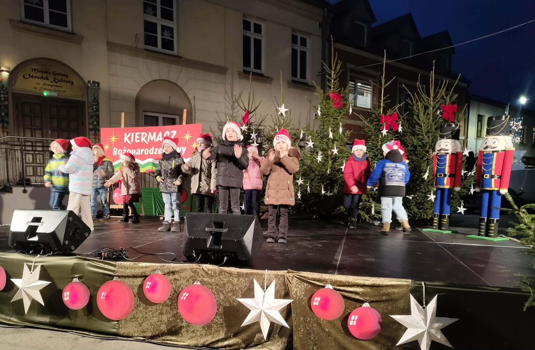 2) Zdjęcie przedstawia występy dzieci podczas kiermaszu bożonarodzeniowego.