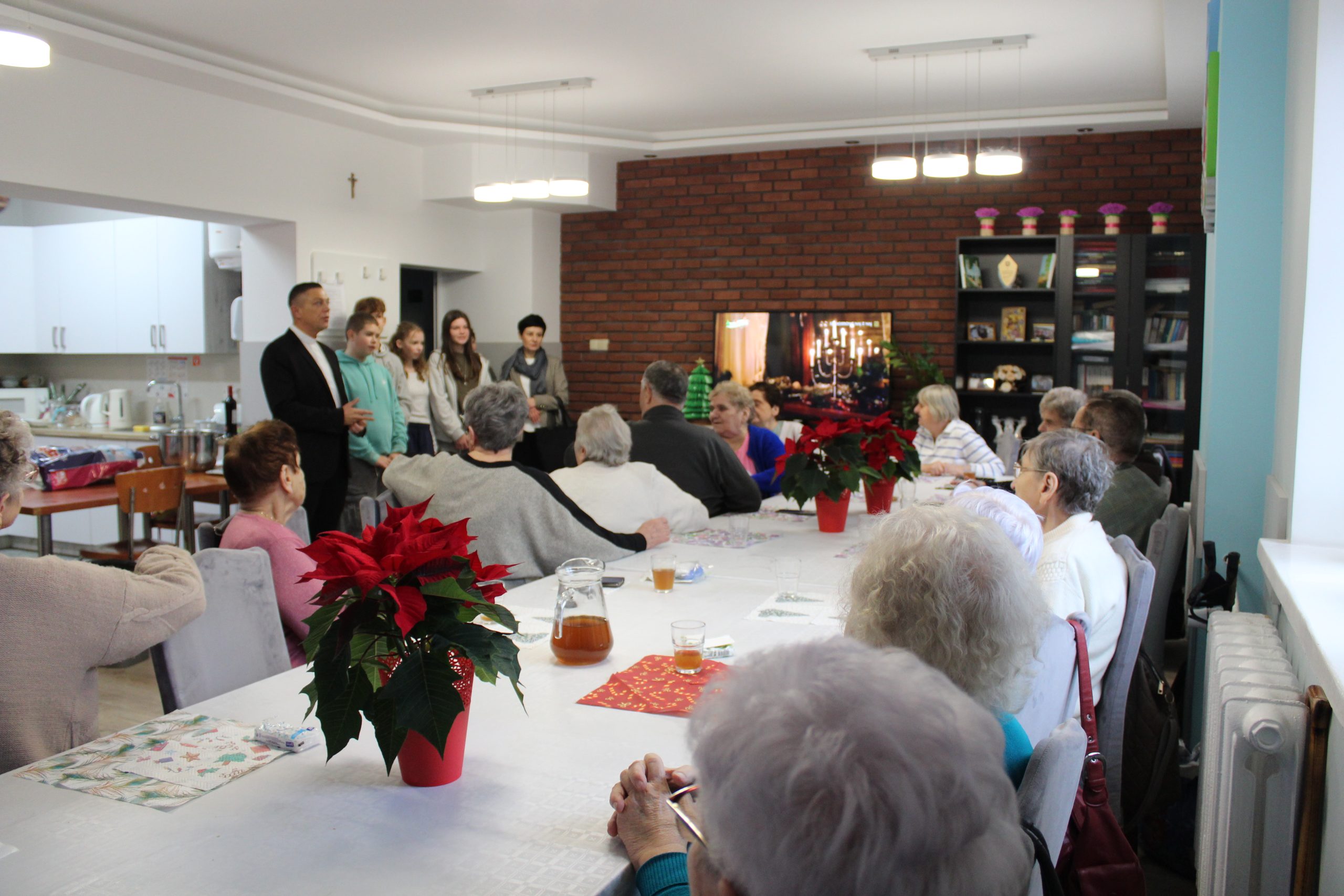 3) Na fotografii seniorzy siedzący przy stole oraz goście wspólnie śpiewający kolędy.