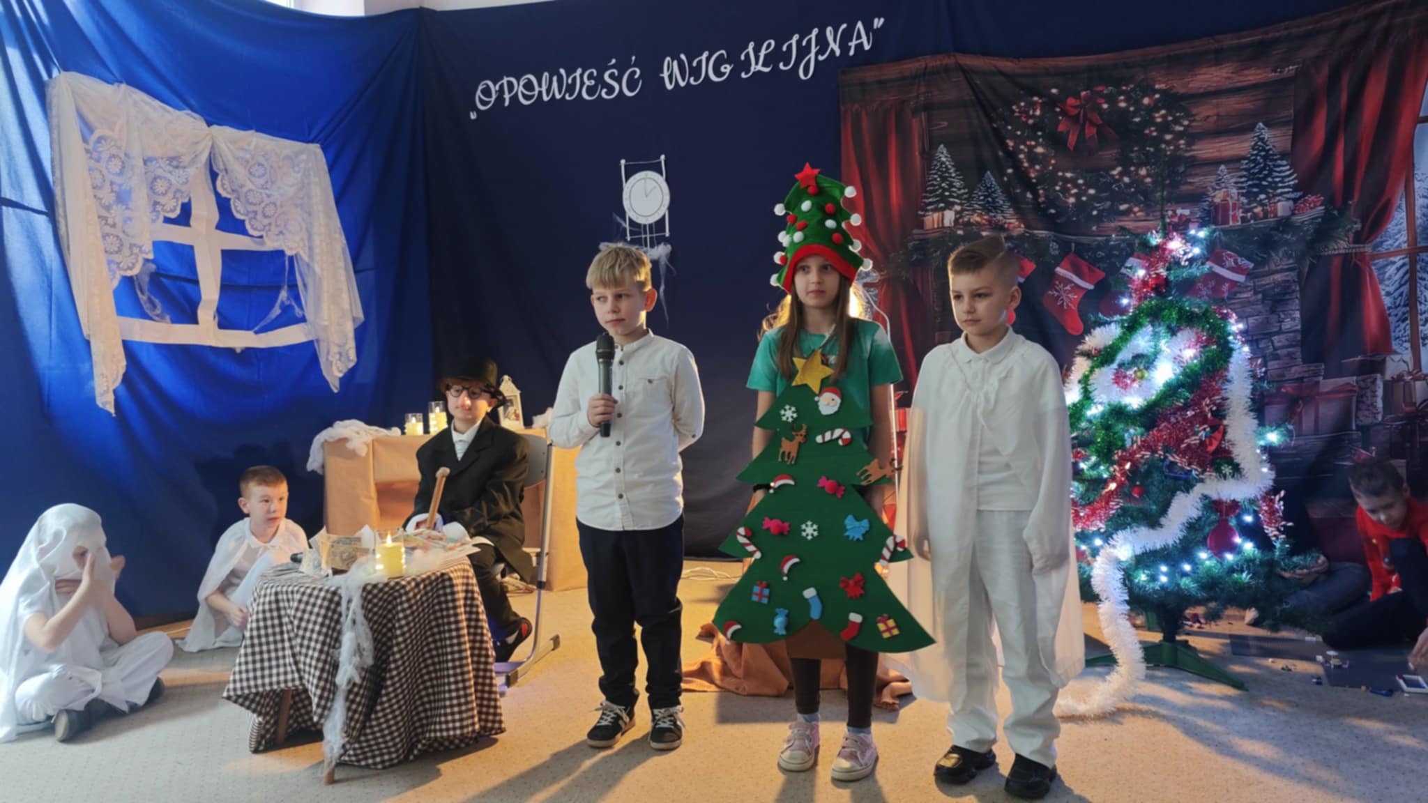 Zdjęcie wykonane na sali, podczas przedstawienia. Przedstawia dzieci na tle świątecznej scenerii