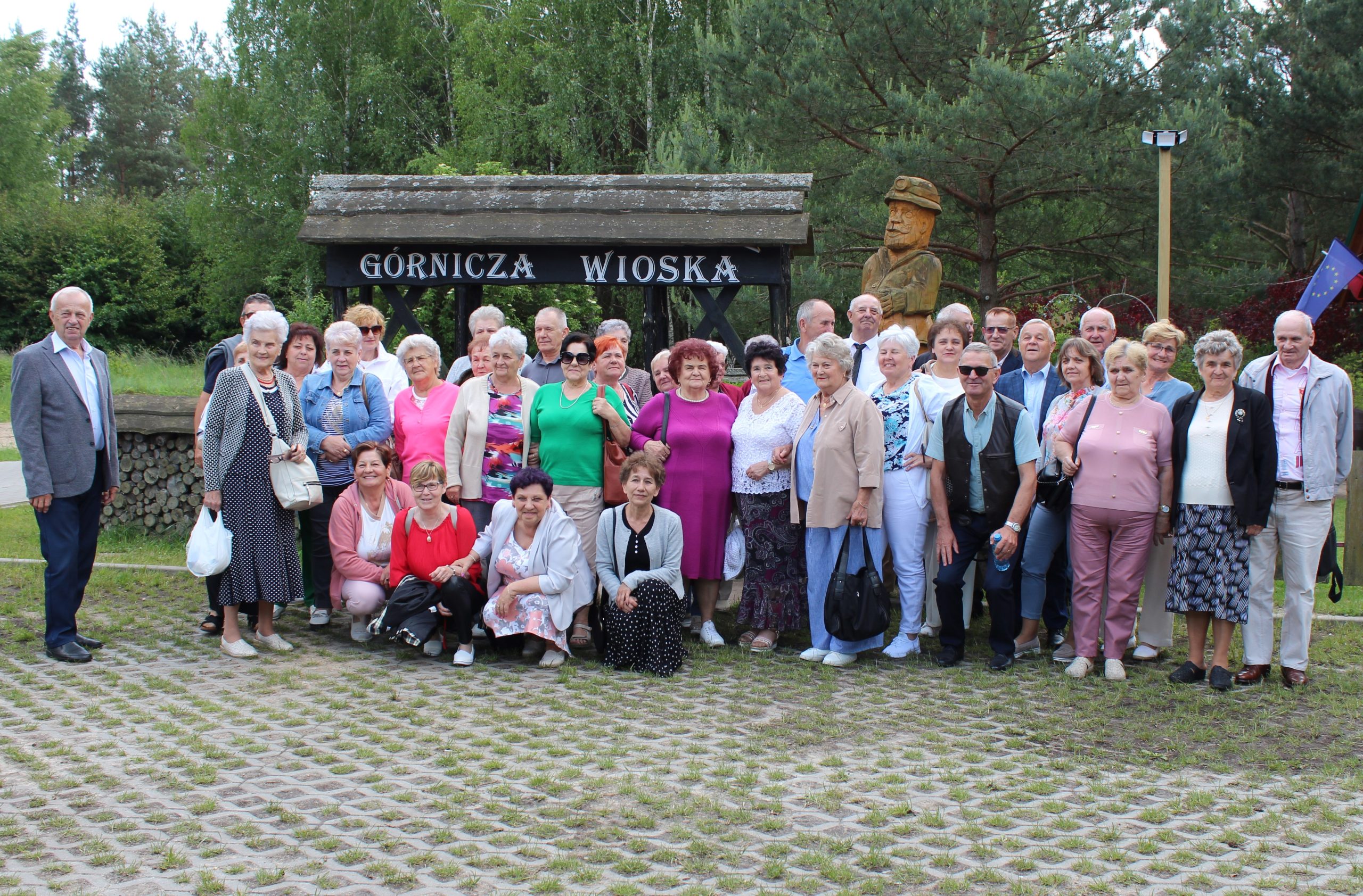 1) Zdjęcie wykonane przed bramą do Górniczej Wioski. Przedstawia seniorów ze ZERiI w Sompolnie oraz uczestników Domu Dziennego Pobytu w Sompolnie. W tle las.
