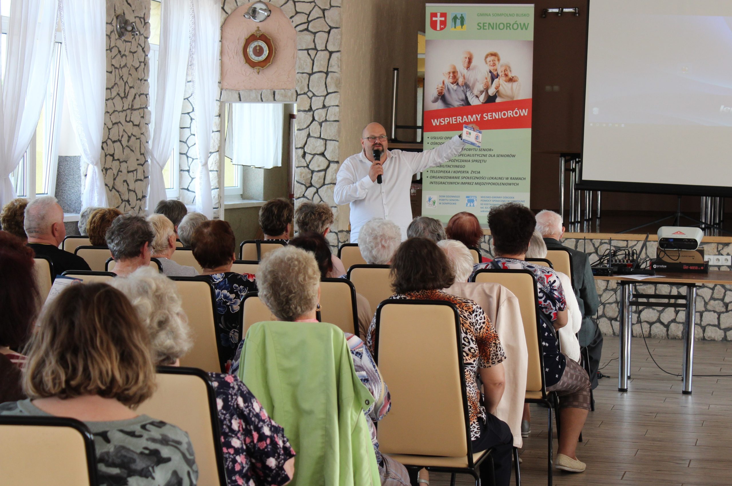 1) Zdjęcie wykonane w sali OSP Sompolno. Przedstawia dyrektora miejsko – Gminnego Ośrodka Pomocy Społecznej w Sompolnie prezentującego Kopertę życia