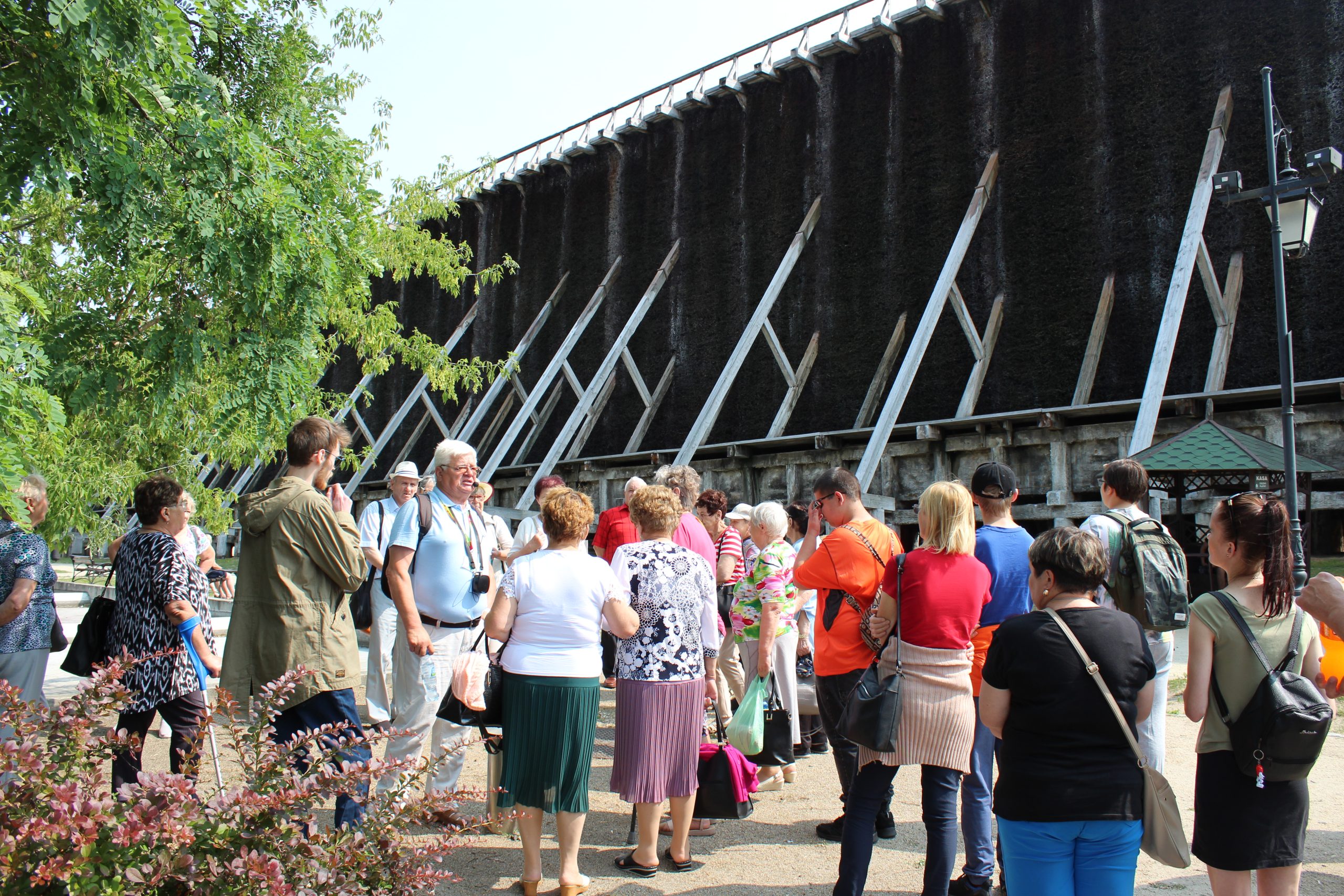 1) Zdjęcie wykonane pod tężniami w Ciechocinku. Widać na nim grupę osób w różnym wieku biorących udział w wycieczce.