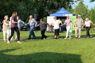 17) Seniorzy i pracownicy MGOPS tańczący na trawie.