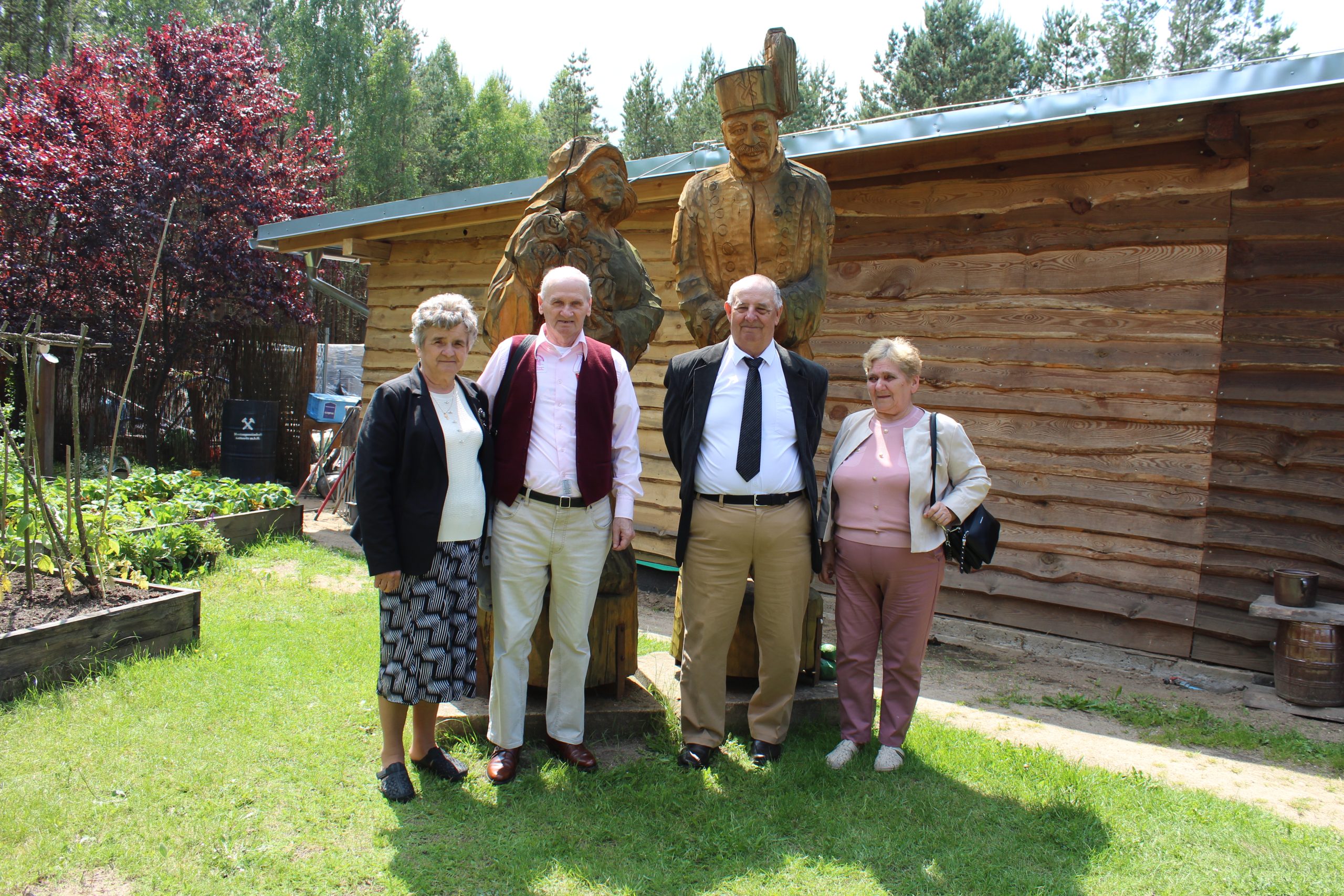 18) Na fotografii czwórka seniorów pozuje do zdjęcia na tle drewnianych figur.