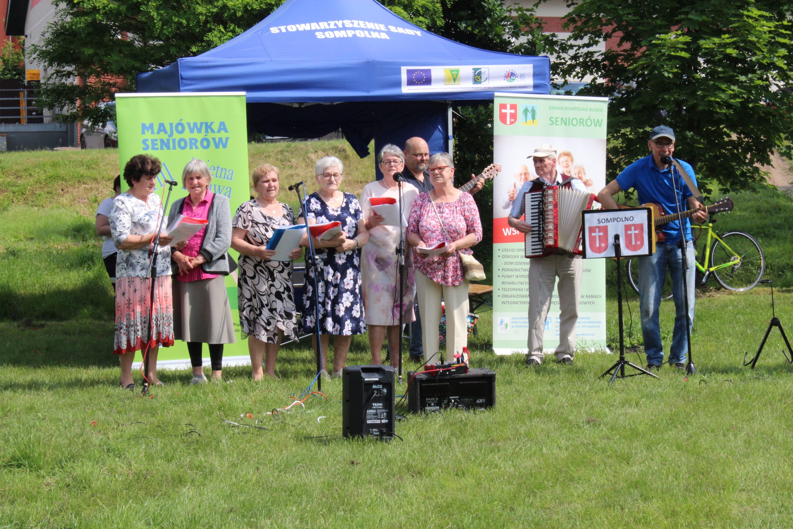 2. Fotografia przedstawia występ seniorów z zespołu muzycznego „Wiecznie Młodzi”, którzy akompaniamencie gitary i akordeonu śpiewają piosenki.