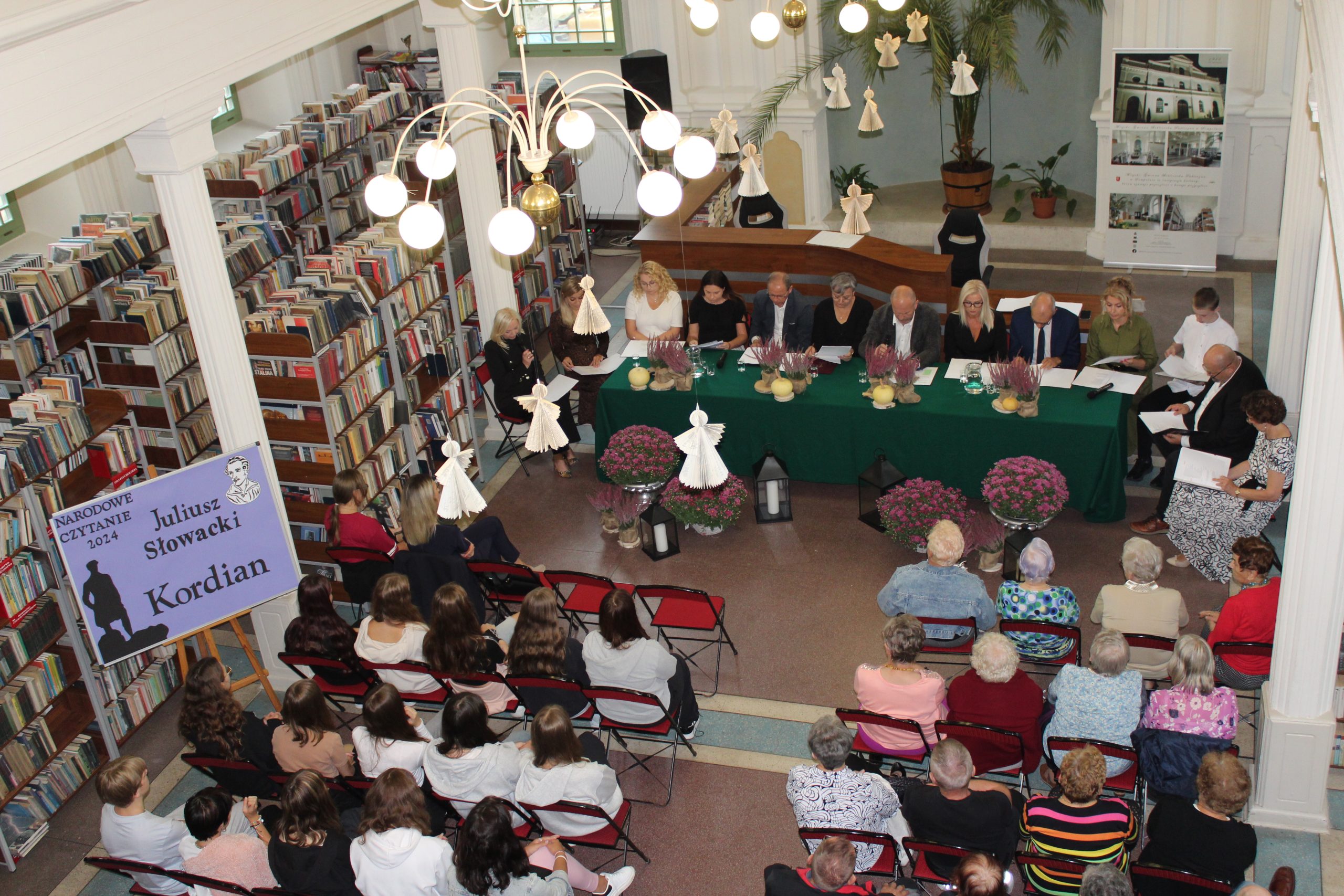 2. Zdjęcie wykonane z góry, ze schodów biblioteki. Przedstawia słuchaczy narodowego czytania oraz lektorów tegorocznej edycji tego wydarzenia.