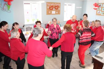 Na fotografii seniorzy i opiekunowie tańczący w kole.