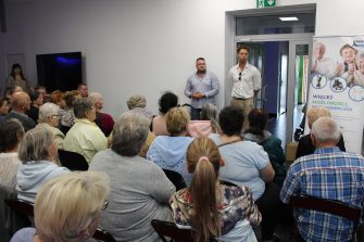 2) Na zdjęciu przedstawiciele Fundacji „Złote lata” opowiadający o celach swojej działalności. Po prawej stronie baner z napisem „Więcej możliwości – mniej ograniczeń”, przed nimi grono osób siedzących na krzesłach.