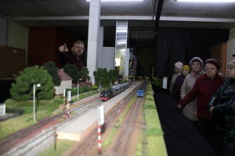 3) Na zdjęciu zbliżenie makiety. W tle osoby uczestniczące w prezentacji oraz właściciel makiety.