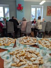 Na fotografii talerze z faworkami a w tle seniorzy siedzący przy stołach