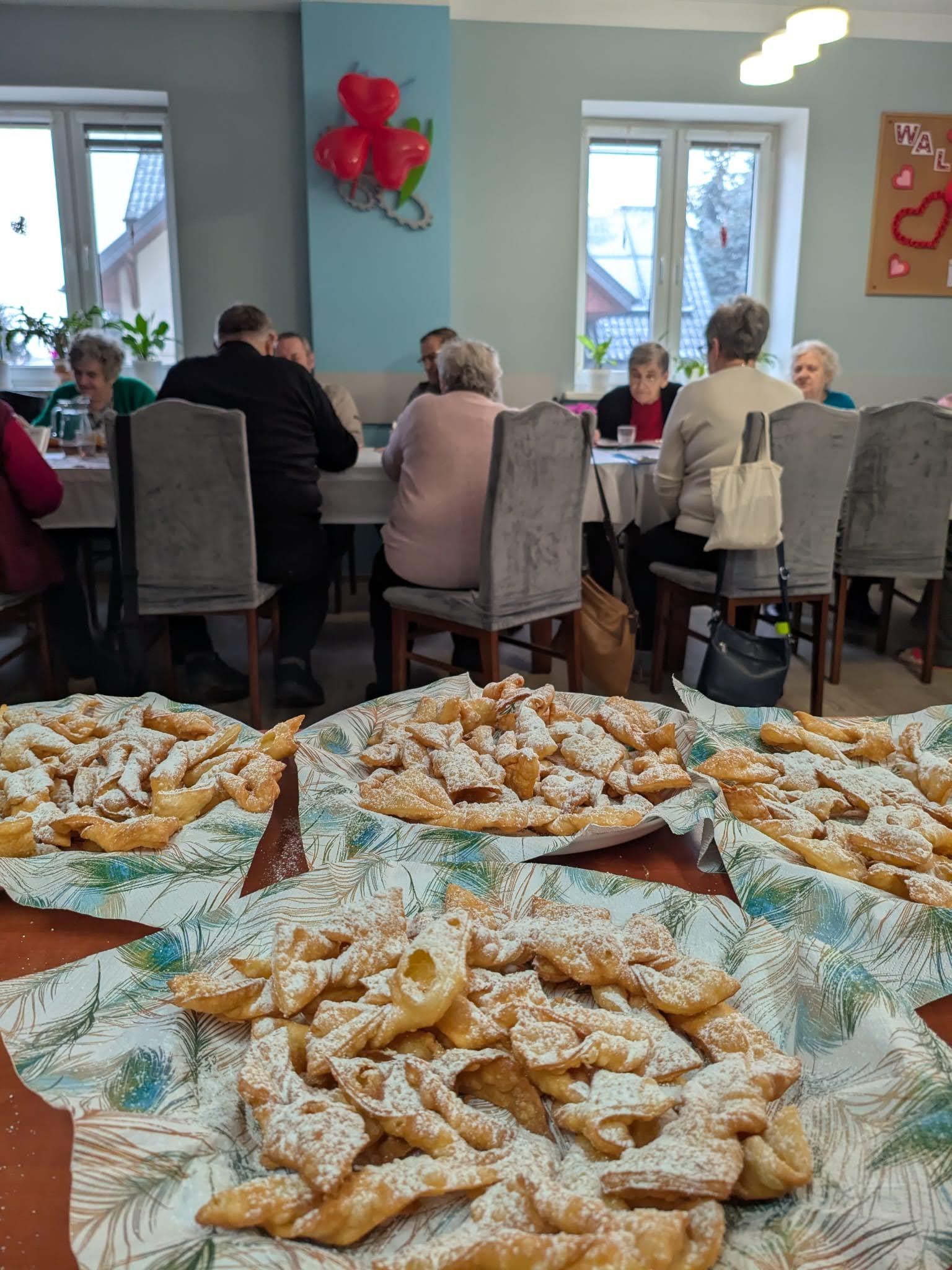 Na fotografii talerze z faworkami a w tle seniorzy siedzący przy stołach