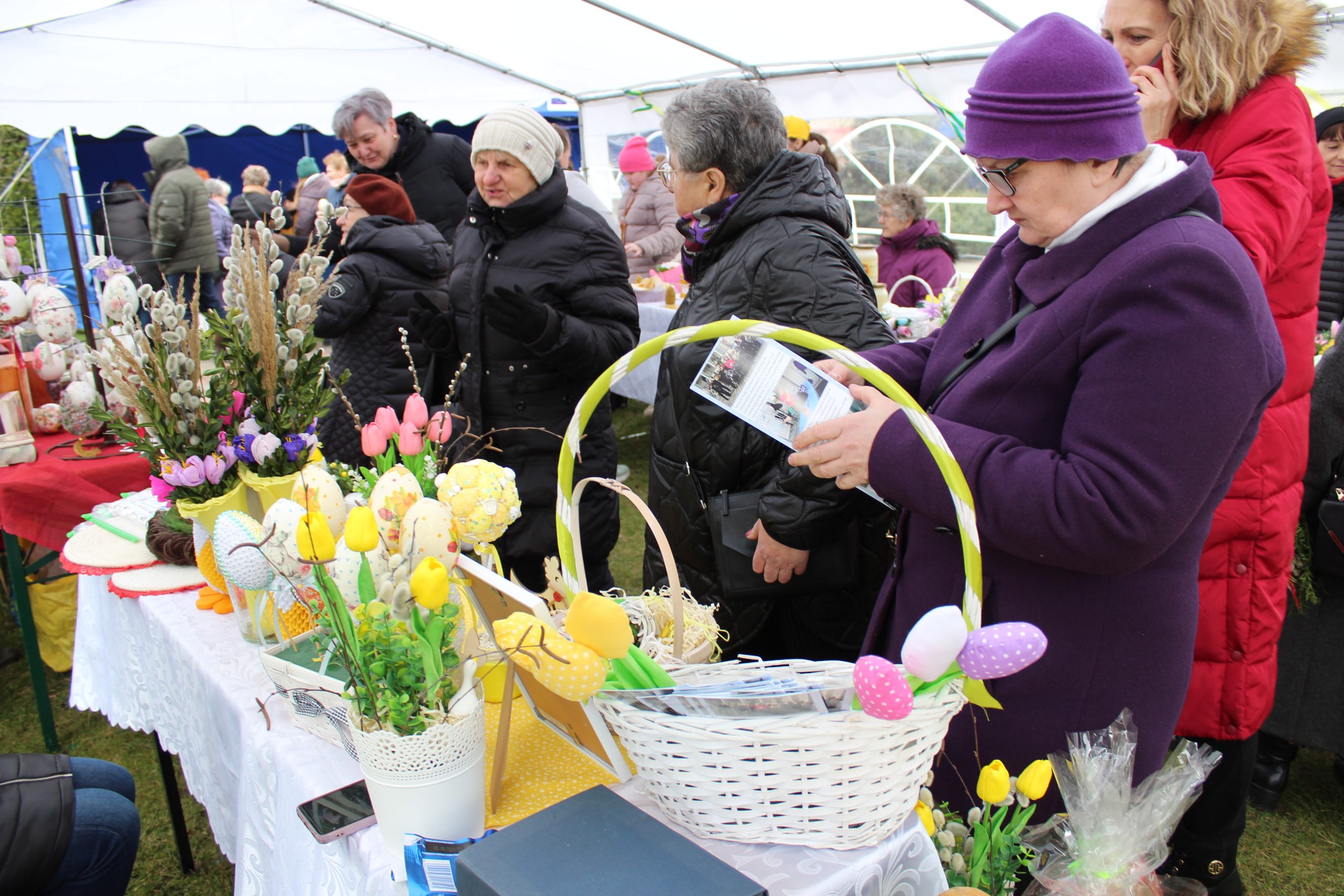4) Zdjęcie przedstawia uczestników Kiermaszu Wielkanocnego oglądających prace wystawione na stoisku.