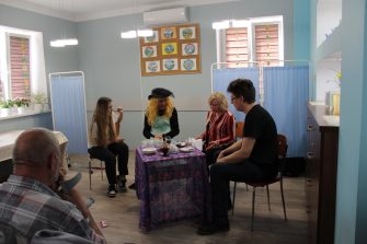 4) Na fotografii czwórka aktorów siedzących przy stoliku na którym stoi karafka, kieliszki i talerzyki.