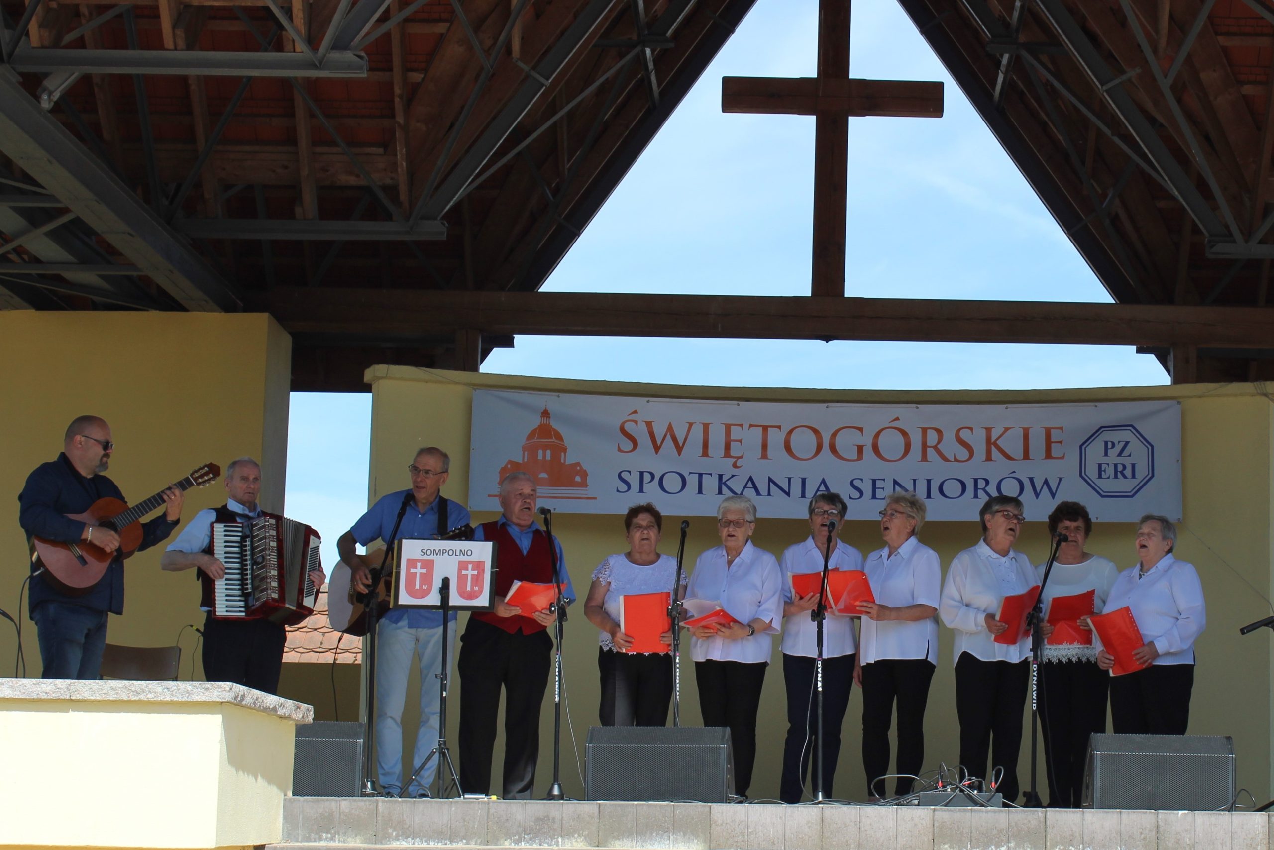 4) Na zdjęciu seniorzy na scenie plenerowej w Świętej Górze. Po lewej stronie dyrektor mgops grający na gitarze, uczestnik ddp grający na akordeonie oraz instruktor muzykoterapii grający na gitarze.