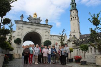 5) Na fotografii seniorzy na tle bramy wiodącej na Jasną Górę