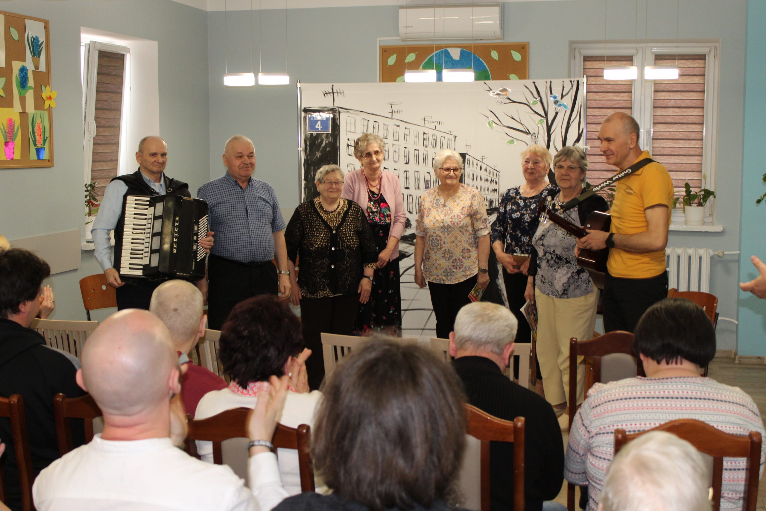 5) Zdjęcie przedstawia ośmioro aktorów grających w sztuce. Publiczność bije brawa.