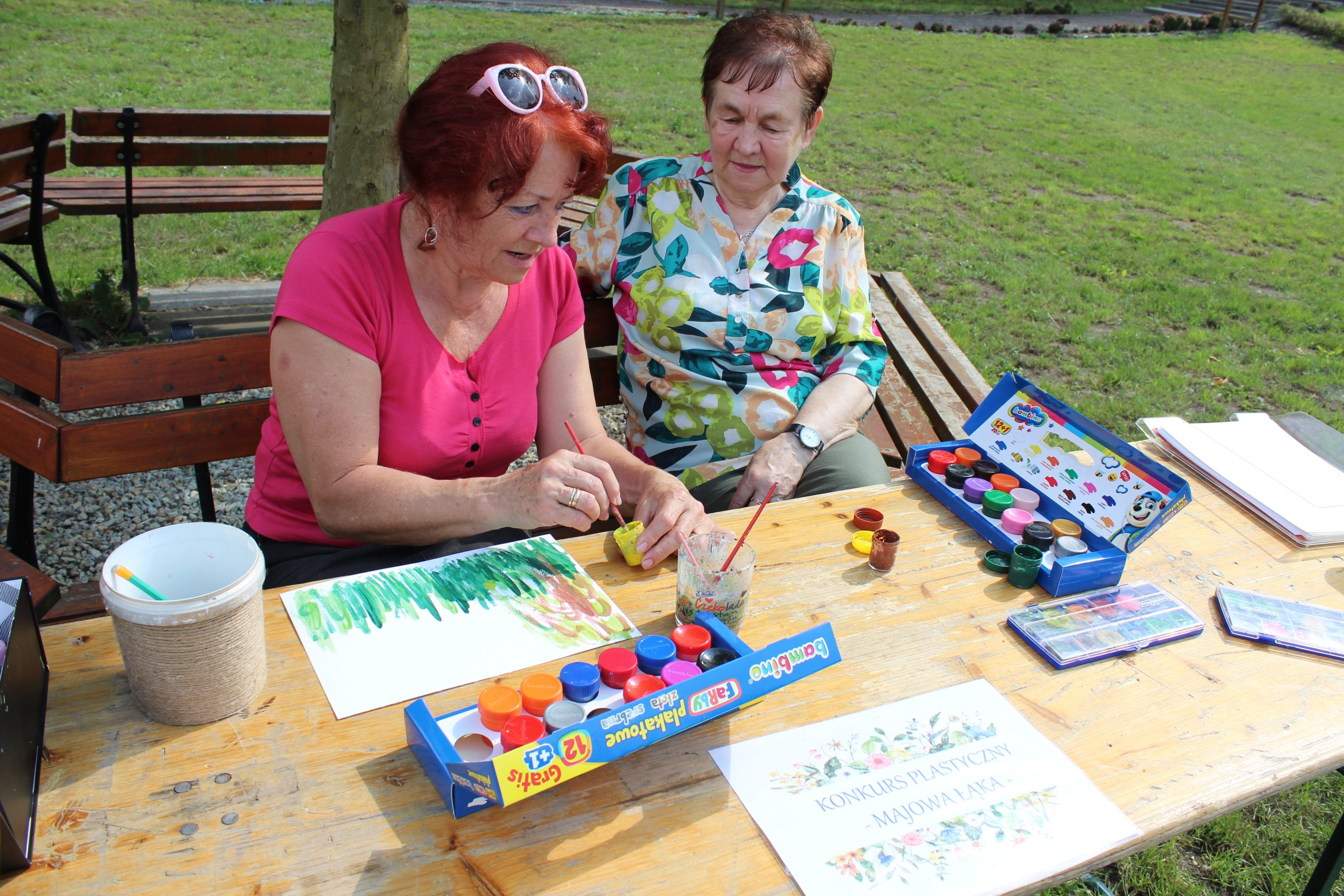 6. Zdjęcie wykonane w parku, przedstawia dwie seniorki malujące pracę plastyczną podczas konkursu przeprowadzonego na Majówce Seniorów.