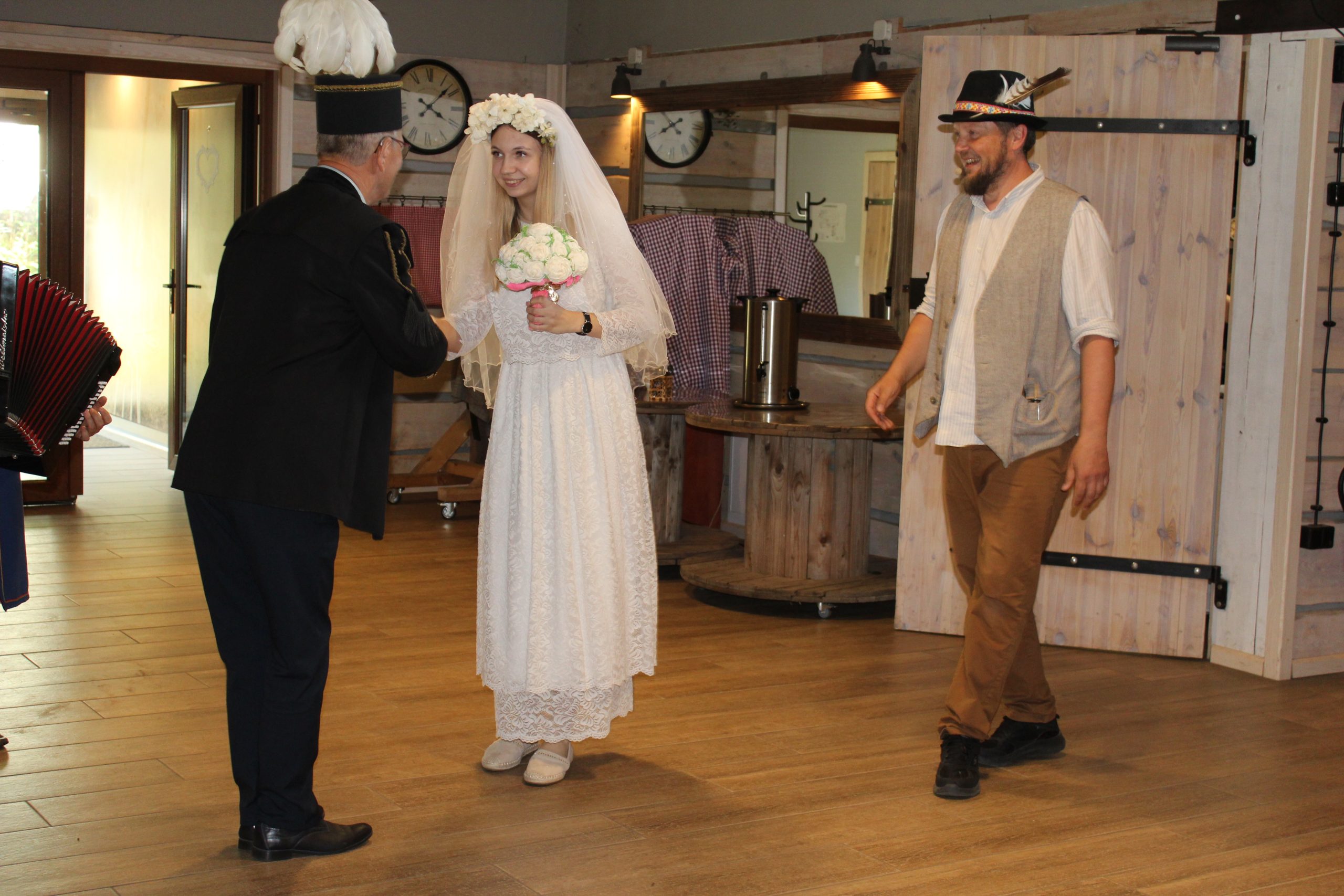 8) Na fotografii dwaj mężczyźni oraz piękna, młoda dziewczyna przebrana za pannę młodą.