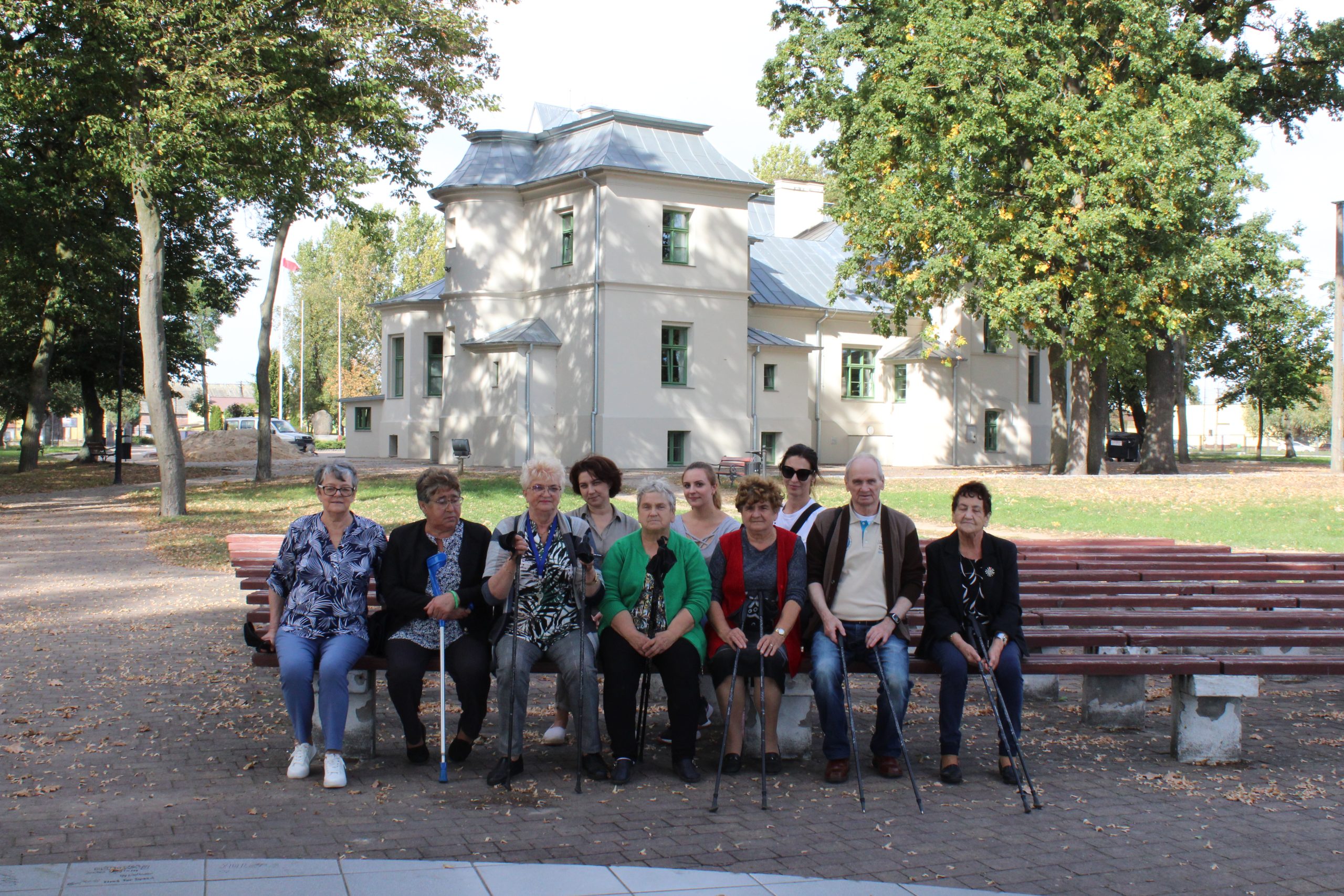 Zdjęcie przedstawia uczestników spaceru z kijami siedzących na tle pałacu we Wierzbinku