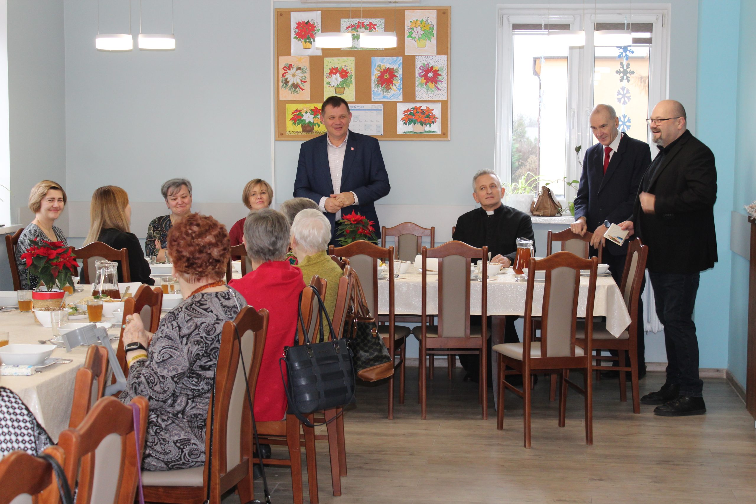 1) Zdjęcie wykonane w sali głównej Domu Dziennego Pobytu dla Osób Starszych w Sompolnie. Przedstawia zaproszonych gości oraz seniorów obecnych na spotkaniu wigilijnym.