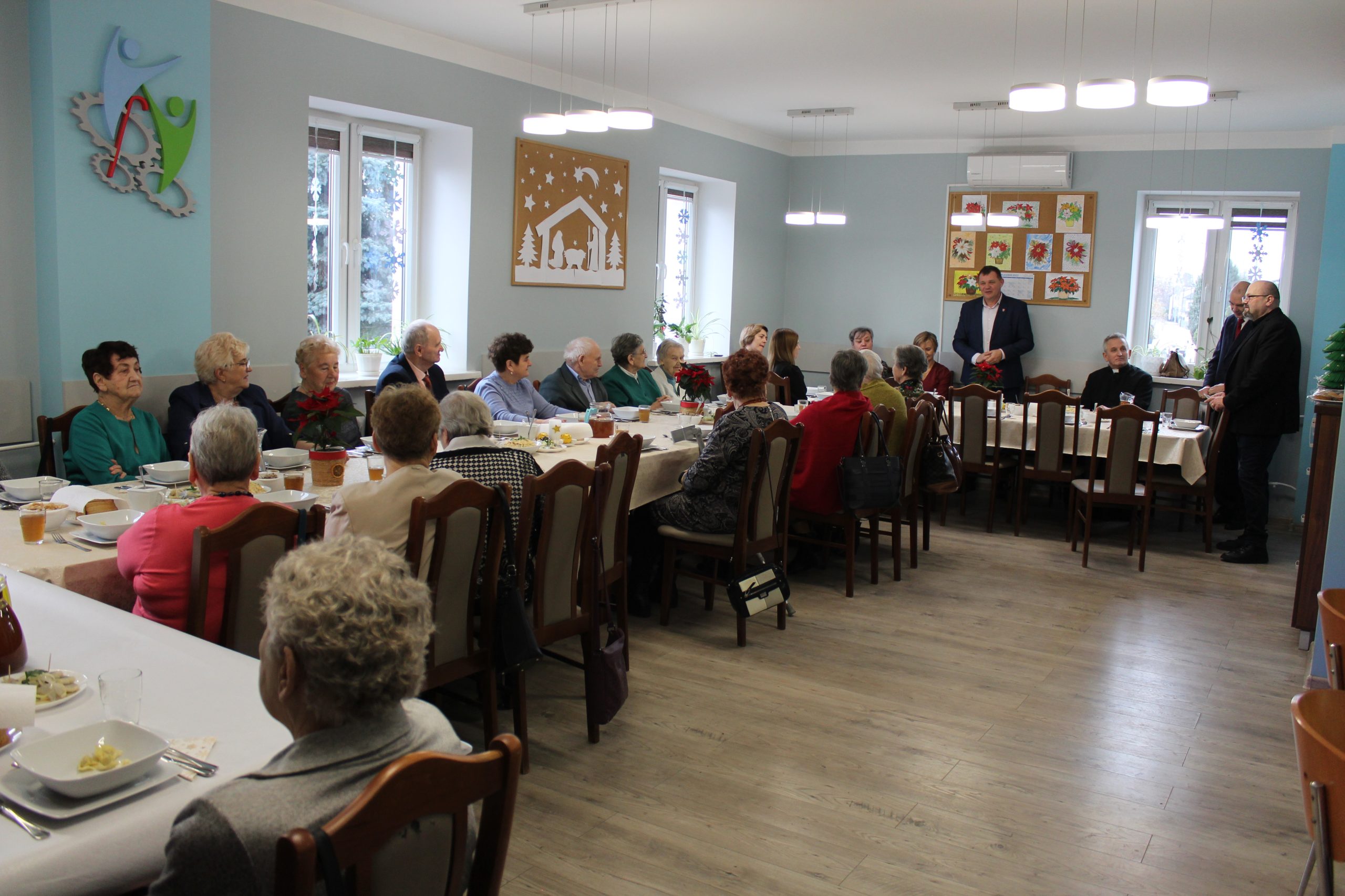 3) Na fotografii wszyscy goście oraz seniorzy siedzący przy stołach w Domu Dziennego Pobytu. Do zebranych przemawia burmistrz oraz dyrektor mgops w Sompolnie