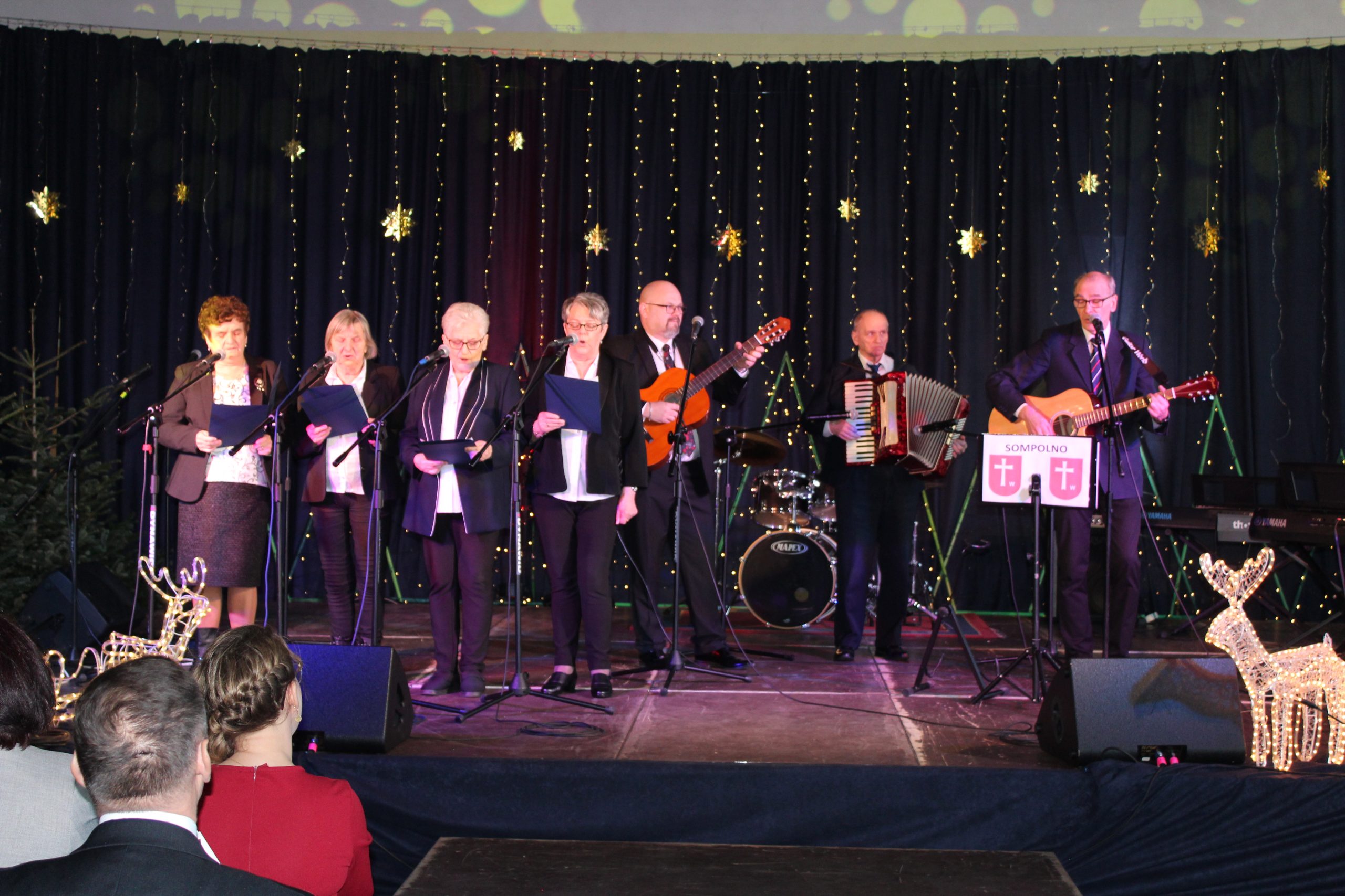 2) Na zdjęciu reprezentacja domu dziennego pobytu. Za nimi rozciąga się granatowa kotara ze złotymi gwiazdami.