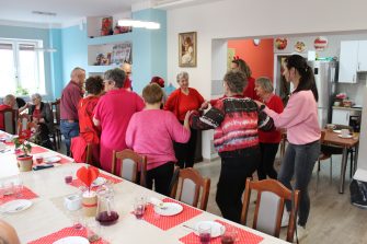 3) Zdjęcie przedstawia seniorów wraz z opiekunami tańczących w kółku.