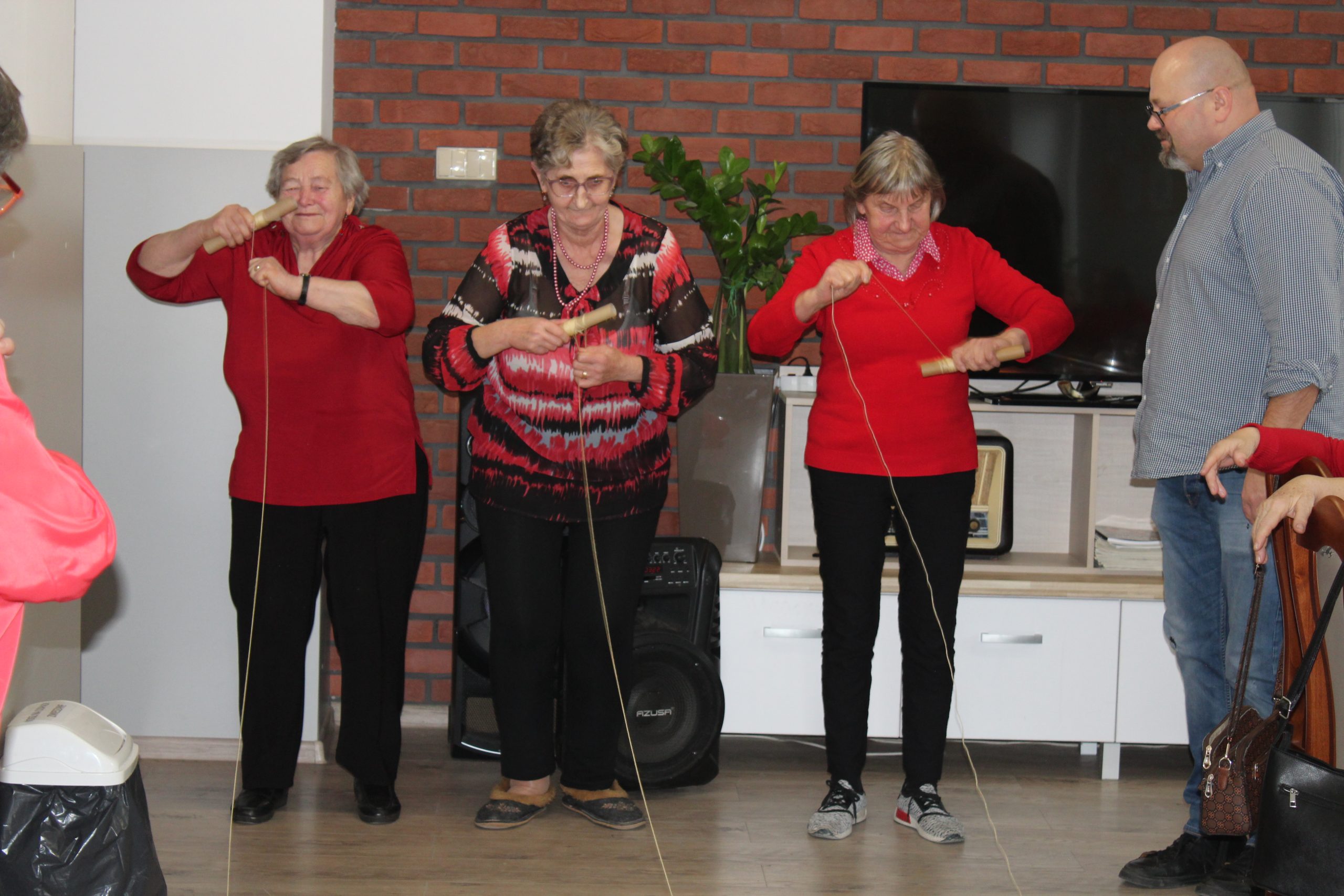 9) Zdjęcie przedstawia kolejne trzy seniorki biorące udział w zabawie – nawijanie balonowego serduszka na sznurku na drążek.