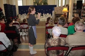 1) Zdjęcie wykonane w miejsko – gminnej bibliotece publicznej w Sompolnie. Przedstawia dziewczynę chodzącą wśród publiczności z mikrofonem w dłoni. W tle scenografia do spektaklu „Dziewczynka z zapałkami”.