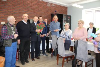 1) Zdjęcie wykonane w Domu Dziennego Pobytu. Przedstawia mężczyzn składających życzenia kobietom.