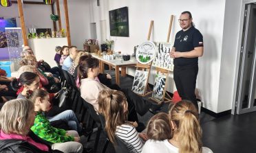 1) Zdjęcie wykonane w sali głównej Dziennego Centrum Wsparcia. Na fotografii przedstawiciel Fundacji Skrzydła Lasu wita zebranych na prezentacji.