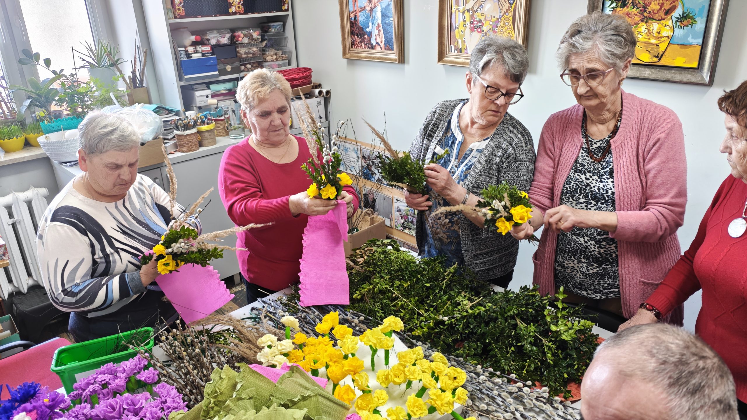 4) Fotografia wykonana w pracowni plastycznej. Przedstawia seniorki wykonujące palmy wielkanocne.