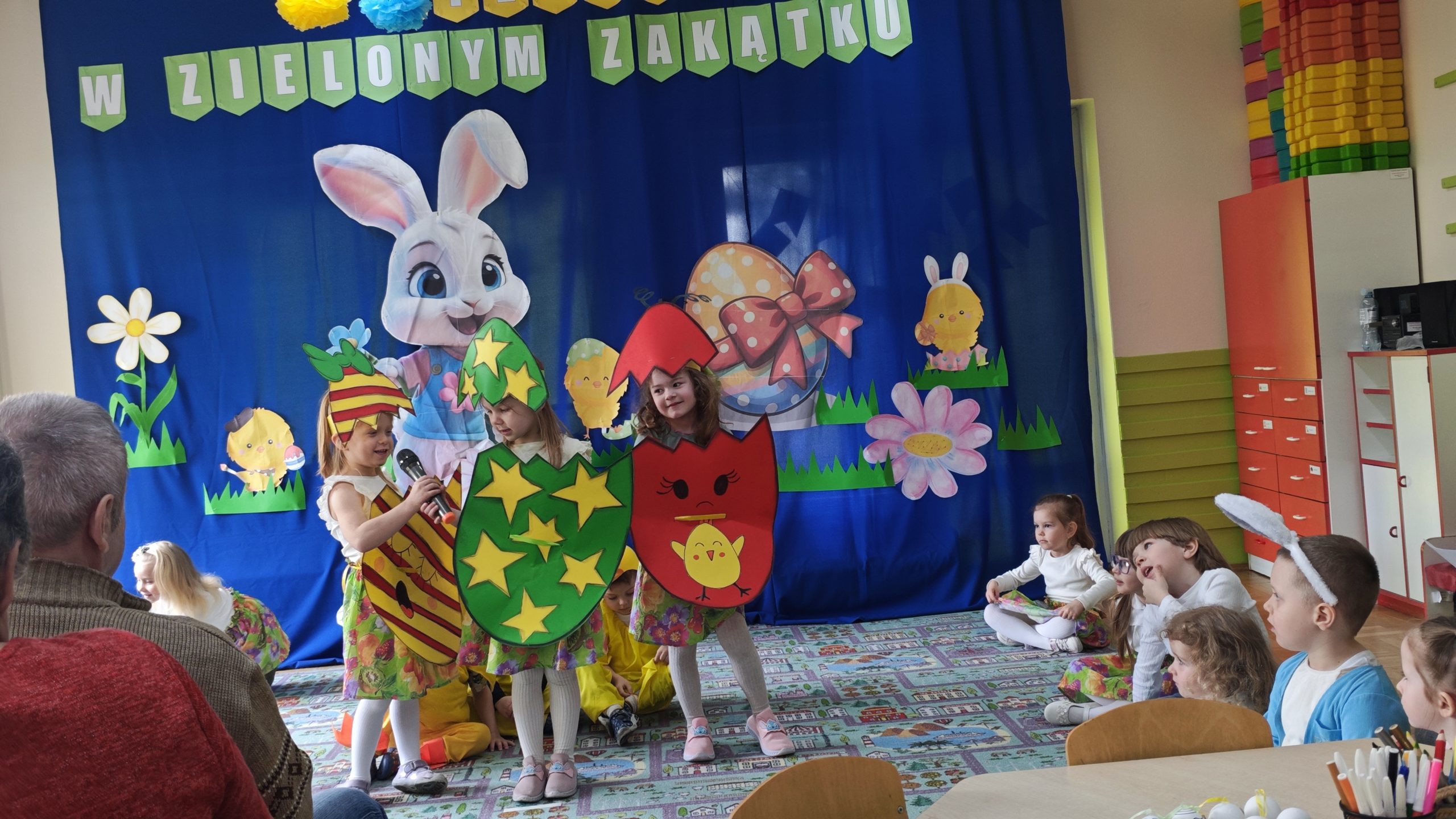 7. Na fotografii widzimy trójkę dzieci przebranych w wielkanocne stroje pisanek, którzy mówią wierszyki podczas występu.