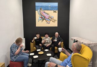 Fotografia przedstawia osoby z DCW pijące kawę pod obrazem autorstwa Pana Tomasza Majewskiego