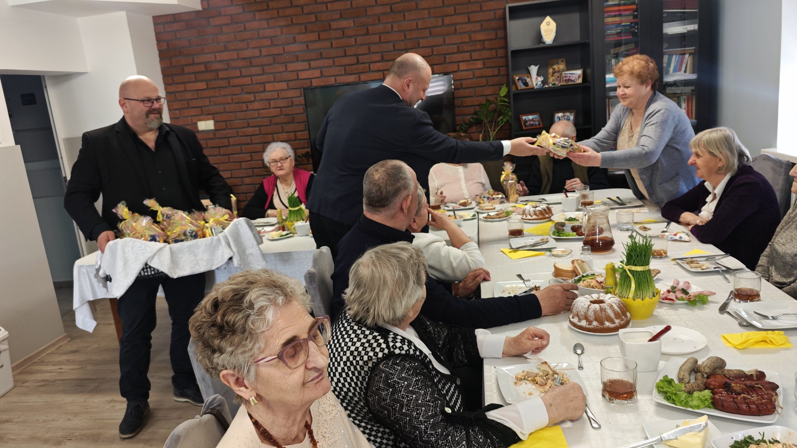 3. Fotografia przedstawia Pana Waldemara Marciniaka wręczającego seniorom słodki upominek z okazji nadchodzących Świąt Wielkanocnych
