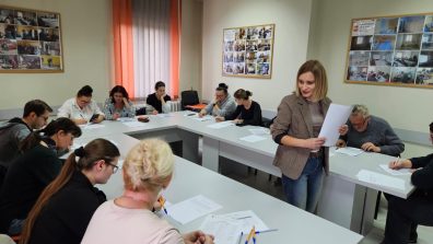 Fotografia przedstawia uczestników szkolenia pracujących nad dokumentami oraz pracownicę M-GOPS w Sompolnie objaśniającą kwestie niejasne dla kursantów